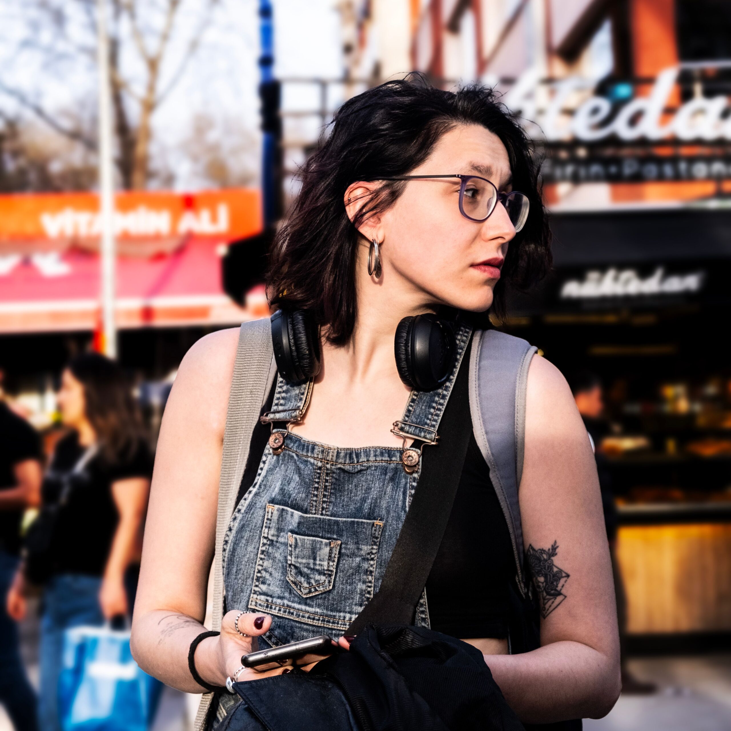 Woman in sunglasses and denim overalls exploring city streets with headphones in Ankara, Türkiye.